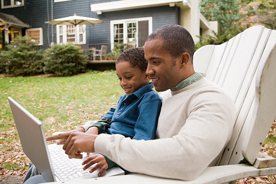 Client Center - Father and Son Using Laptop in Front of Home