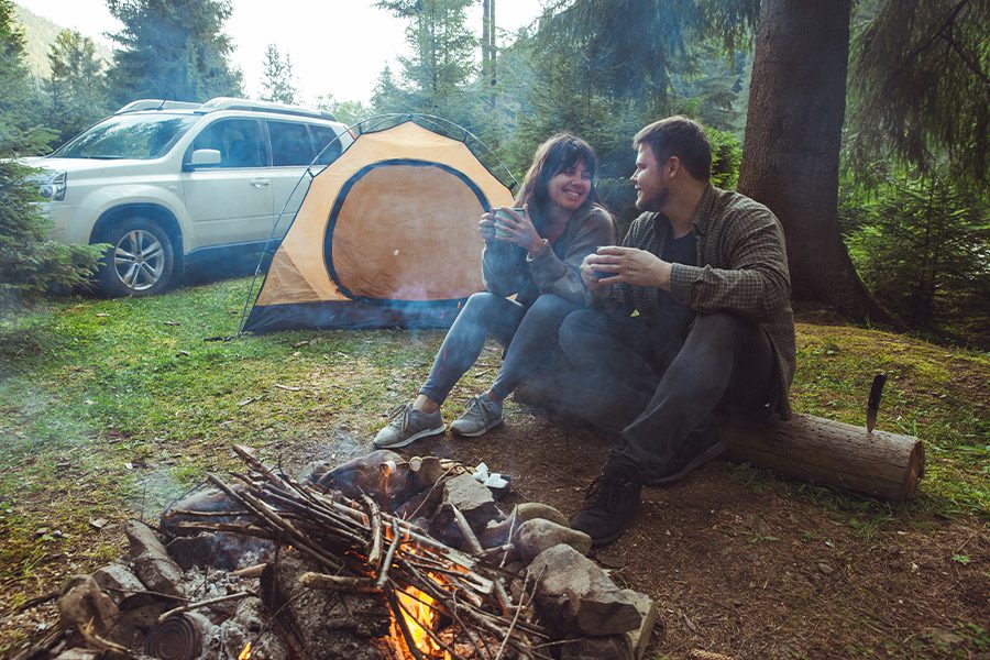 Contact - Couple Sitting Near Camp Fire and Drinking Tea Outdoors